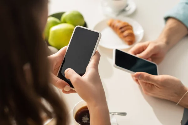 Foco seletivo da mulher segurando smartphone perto do namorado durante o café da manhã na cozinha — Fotografia de Stock