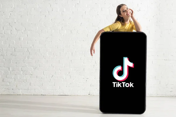 KYIV, UKRAINE - 21 février 2020 : Femme positive regardant la caméra près de l'application TikTok sur le modèle de smartphone — Photo de stock