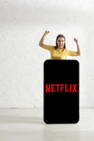 KIEW, UKRAINE - 21. FEBRUAR 2020: Positive Frau zeigt Ja-Geste in der Nähe der Netflix-App auf dem Smartphone-Modell — Stockfoto