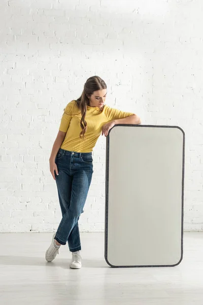 Ragazza attraente guardando grande modello di smartphone vicino muro di mattoni bianchi — Foto stock