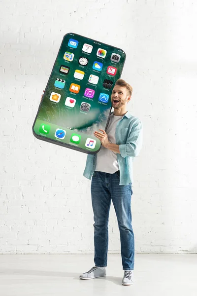 KYIV, UCRANIA - 21 de febrero de 2020: Hombre feliz sosteniendo gran modelo de teléfono inteligente con pantalla de iphone - foto de stock