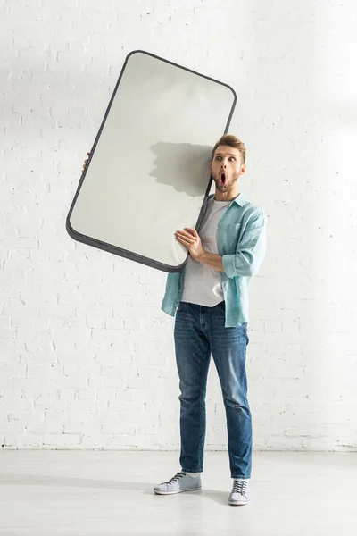 Shocked uomo in possesso di modello di smartphone vicino muro di mattoni bianchi — Foto stock