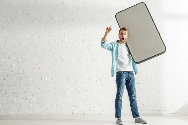 Aufgeregter Mann hat Idee, während er Modell des Smartphones zu Hause hält — Stockfoto