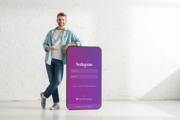 KYIV, UKRAINE - FEBRUARY 21, 2020: Handsome man smiling at camera and pointing on model of smartphone with instagram app — Stock Photo
