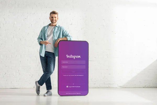 KYIV, UKRAINE - 21 FÉVRIER 2020 : Beau homme souriant à la caméra et pointant sur le modèle de smartphone avec application instagram — Photo de stock