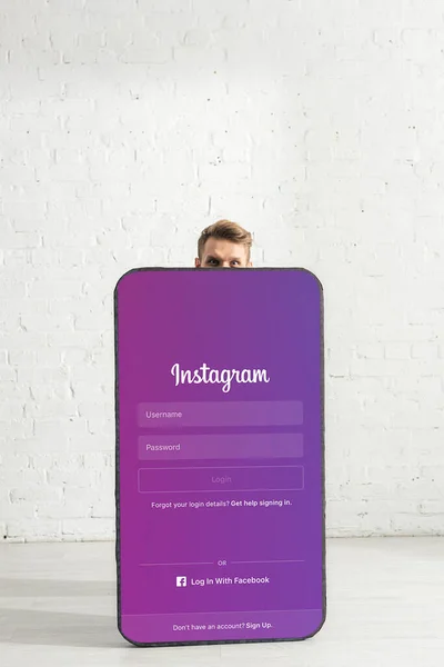 KIEW, UKRAINE - 21. FEBRUAR 2020: Mann blickt mit Instagram-App auf Kamera in der Nähe eines großen Smartphone-Modells — Stockfoto