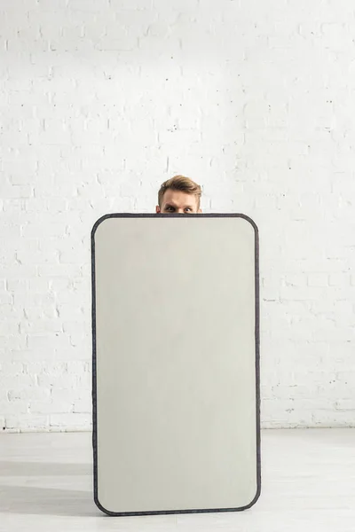 Hombre mirando la cámara cerca de modelo grande de teléfono inteligente en casa - foto de stock