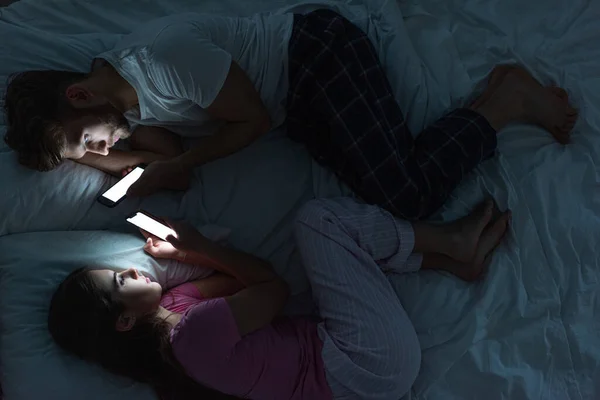 Top view of couple lying on bed with smartphones at night — Stock Photo