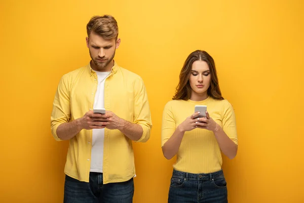 Pareja joven usando teléfonos inteligentes sobre fondo amarillo - foto de stock