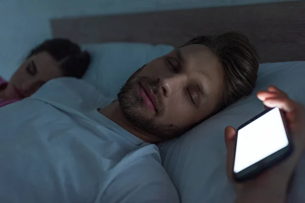 Selektiver Fokus des Smartphones: Mann schläft nachts neben Freundin im Bett — Stockfoto