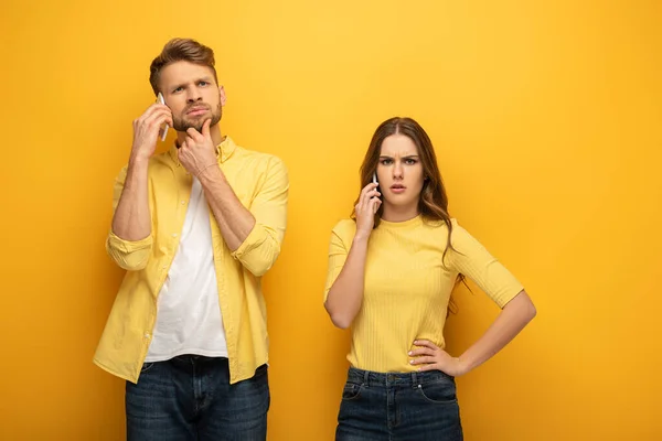 Couple confus parlant sur les smartphones sur fond jaune — Photo de stock