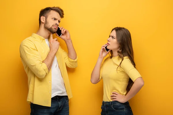 Skeptical couple talking on smartphones on yellow background — Stock Photo