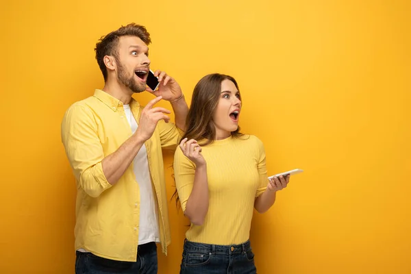 Coppia eccitata con smartphone guardando lontano su sfondo giallo — Foto stock