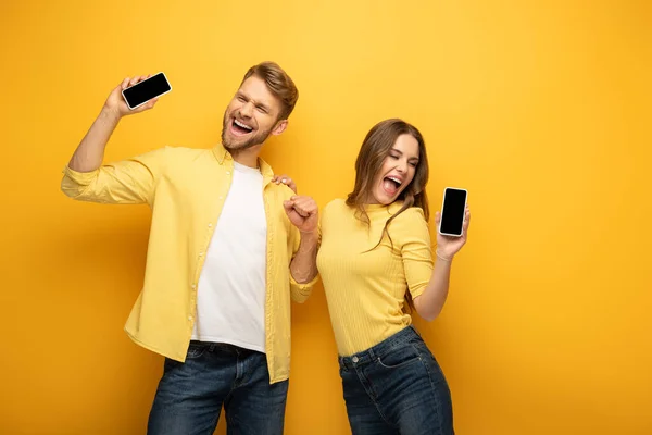 Cheerful young couple holding smartphones with blank screens on yellow background — Stock Photo