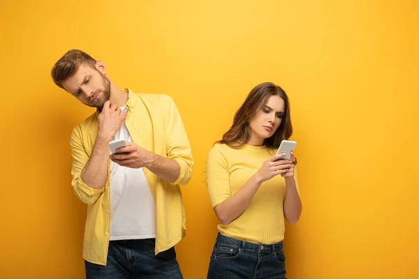 Pensive couple using smartphones on yellow background — Stock Photo