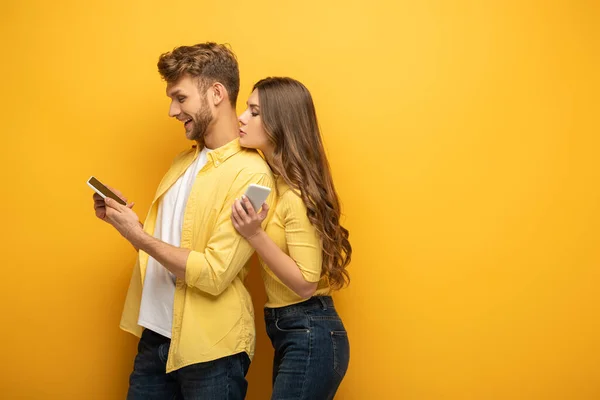 Side view of young couple looking at smartphone on yellow background — Stock Photo