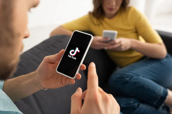 KYIV, UKRAINE - FEBRUARY 21, 2020: Selective focus of man holding smartphone with TikTok app near woman at home — Stock Photo