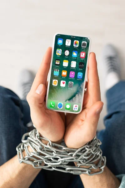 KYIV, UKRAINE - FEBRUARY 21, 2020: Top view of man with tied hands with metal chain holding smartphone with iphone screen — Stock Photo