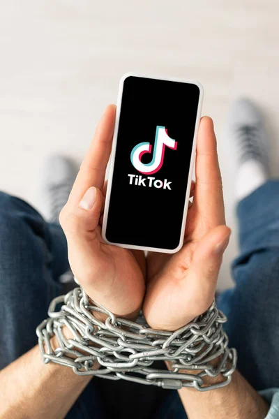 KYIV, UKRAINE - FEVEREIRO 21, 2020: Visão superior do homem segurando smartphone com aplicativo TikTok em mãos atadas com corrente de metal — Fotografia de Stock