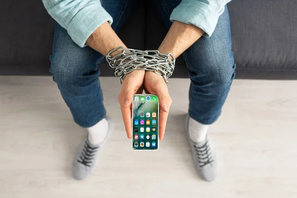 KYIV, UCRANIA - 21 de febrero de 2020: Vista superior del hombre sosteniendo el teléfono inteligente con pantalla de iphone en manos atadas con cadena de metal - foto de stock