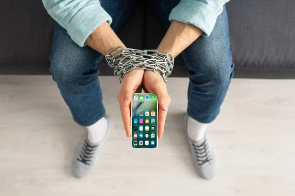 KYIV, UKRAINE - FEBRUARY 21, 2020: Top view of man holding smartphone with iphone screen in linked hand with metal chain — стокове фото