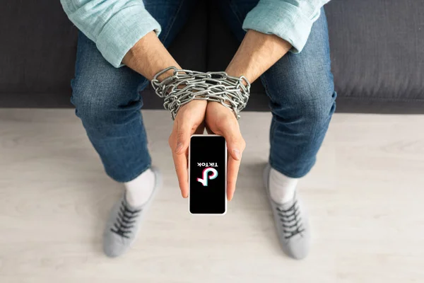 KYIV, UKRAINE - FEBRUARY 21, 2020: Top view of man with metal chain around hands holding smartphone with TikTok app on couch — Stock Photo