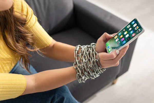 KYIV, UKRAINE - FEBRUARY 21, 2020: Cropped view of woman with metal chain around hands holding smartphone with iphone screen — Stock Photo