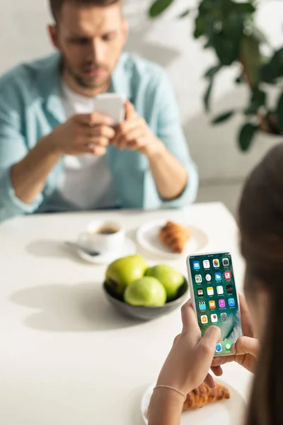 KYIV, UKRAINE - FEBRUARY 21, 2020: Selective focus of woman using smartphone with iphone screen near boyfriend and breakfast on table — Stock Photo