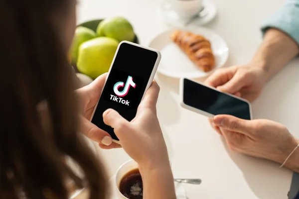 KYIV, UKRAINE - 21 FÉVRIER 2020 : Mise au point sélective de la femme tenant un smartphone avec application TikTok près de l'homme petit déjeuner sur la table dans la cuisine — Photo de stock