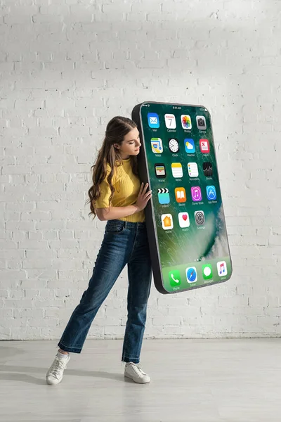 KYIV, UCRANIA - 21 de febrero de 2020: Atractiva chica sosteniendo el modelo de teléfono inteligente con pantalla de iphone en casa - foto de stock