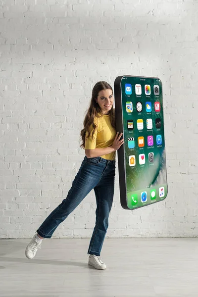 KYIV, UKRAINE - FEBRUARY 21, 2020: Woman smiling at camera while holding model of smartphone with iphone screen — Stock Photo