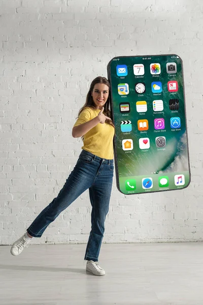 KYIV, UKRAINE - FEBRUARY 21, 2020: Smiling woman pointing with finger at big model of smartphone with iphone screen — Stock Photo