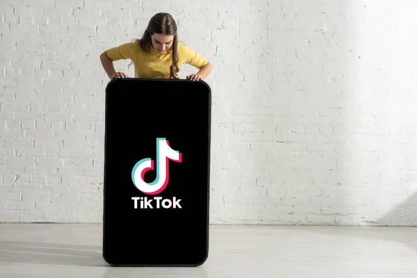 KYIV, UKRAINE - FEBRUARY 21, 2020: Жінка дивиться на велику модель смартфона з додатком TikTok вдома — стокове фото