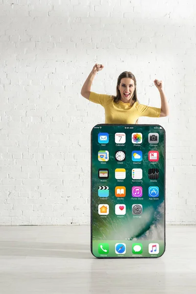 KYIV, UKRAINE - FEBRUARY 21, 2020: Happy woman showing yes gesture near huge model of smartphone with iphone screen — Stock Photo