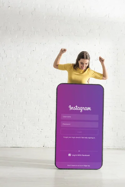 KYIV, UKRAINE - FEBRUARY 21, 2020: Beautiful smiling woman showing yeah gesture and looking at big model of smartphone with instagram app — Stock Photo