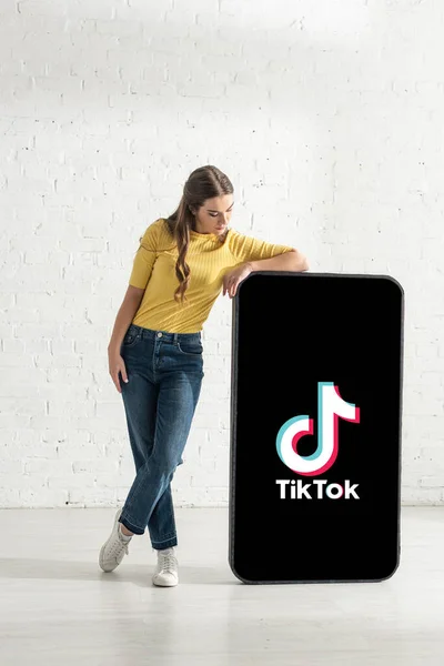 KYIV, UKRAINE - FEBRUARY 21, 2020: Young girl standing near big model of smartphone with TikTok app at home — Stock Photo