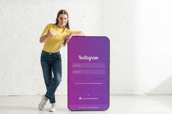 KIEW, UKRAINE - 21. FEBRUAR 2020: Lächelnde Frau zeigt mit dem Finger auf Smartphone-Modell mit Instagram-App — Stockfoto