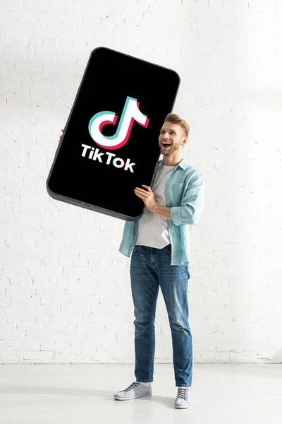 KYIV, UCRANIA - 21 de febrero de 2020: Hombre alegre sosteniendo un enorme modelo de teléfono inteligente con la aplicación TikTok - foto de stock
