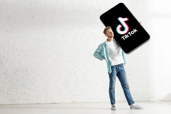 KIEW, UKRAINE - 21. FEBRUAR 2020: Schöner Mann mit riesigem Smartphone-Modell mit TikTok-App in der Nähe weißer Ziegelmauer — Stockfoto