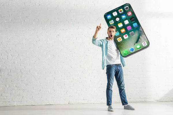 KYIV, UCRAINA - 21 FEBBRAIO 2020: Uomo eccitato che mostra il gesto dell'idea mentre tiene in mano un grande modello di smartphone con schermo iphone — Foto stock