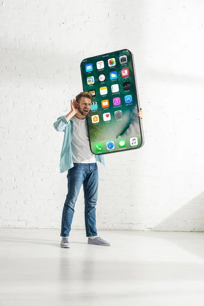 KIEW, UKRAINE - 21. FEBRUAR 2020: Mann mit Hand am Ohr hält großes Smartphone-Modell mit iPhone-Bildschirm — Stockfoto