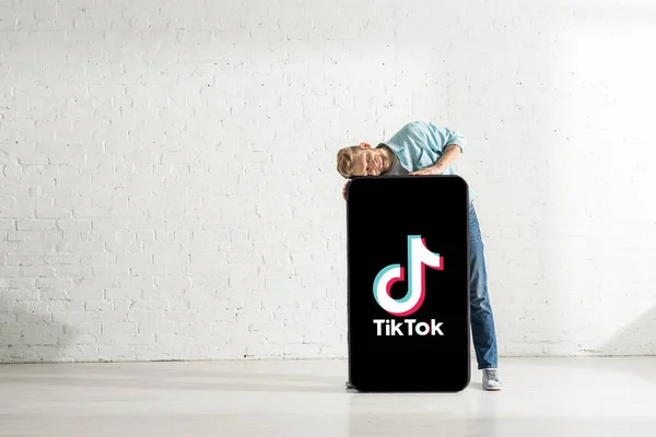 KYIV, UKRAINE - 21 février 2020 : Un homme positif aux yeux fermés étreignant un énorme modèle de smartphone avec l'application TikTok — Photo de stock