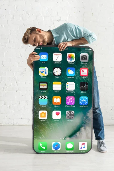 KYIV, UKRAINE - FEBRUARY 21, 2020: Young man kissing big model of smartphone with iphone screen near white brick wall — Stock Photo