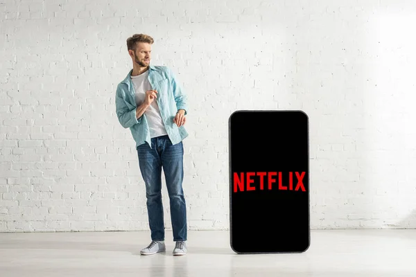 KIEW, UKRAINE - 21. FEBRUAR 2020: Verängstigter Mann steht neben riesigem Smartphone-Modell mit Netflix-App — Stockfoto
