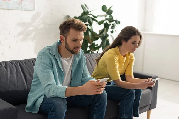 Hombre usando teléfono inteligente cerca de novia charlando en el sofá - foto de stock