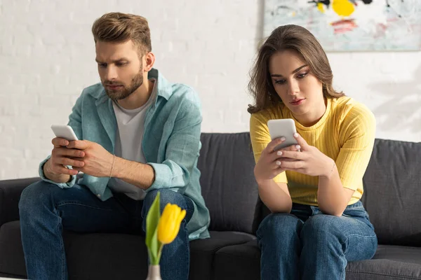 Селективный фокус молодой пары с помощью смартфонов, сидя дома на диване — стоковое фото