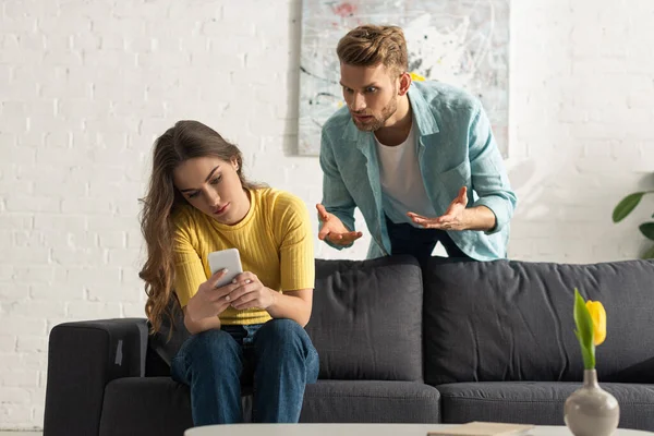 Angry man quarreling at smartphone depended girlfriend on couch — Stock Photo