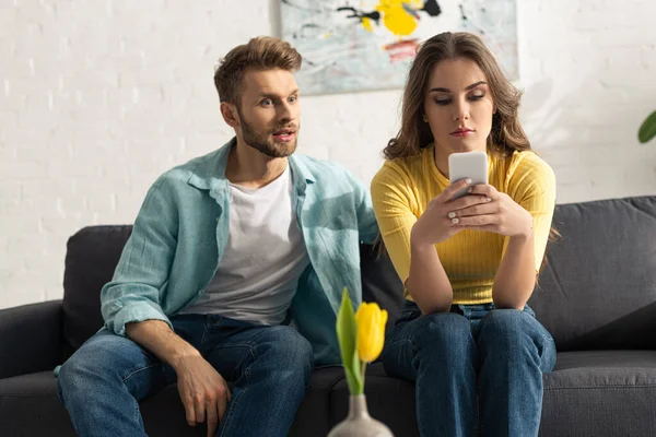 Selective focus of man sitting near smartphone depended girl on couch at home — Stock Photo