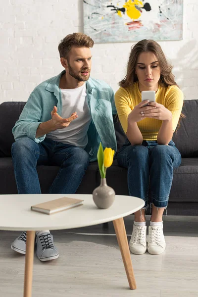 Selective focus of man quarreling with smartphone addicted girlfriend on couch — Stock Photo
