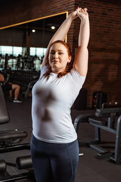 Smiling overweight girl stretching with raised hands and looking at camera — Stock Photo